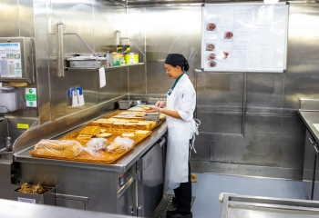 A woman stands in an industrial kitchen with bread making sandwiches