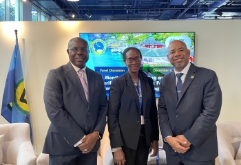 three persons in business suits standing looking into camera, the middle one is a black woman, those flanking are two black men