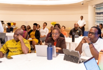 Three people sitting at a desk look on at the launch of the Caribbean Development Bank, InterAmerican Bank US$5.22 million project aimed at increasing the capacity of the public health care system in Saint Lucia to respond to current and emergent health security threats.