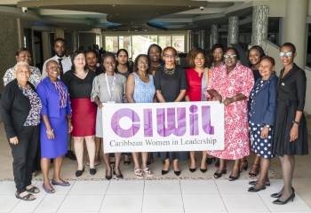 A group of women stand behind a banner with the words CIWIL Caribbean Women in Leadership printed on it 