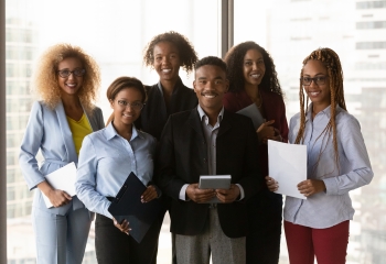 Six black professionals standing in a row holding papers and smiling 