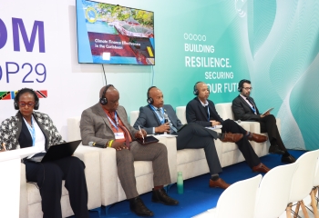 one woman and three men in business suits seated on stage on white lounge chairs 