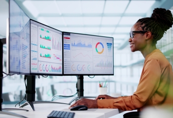 black woman sitting in front of screens smiling and looking at data 