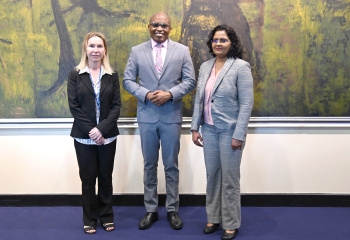 Two women flanking one man all in business suits standing in front a lightly coloured textured wall