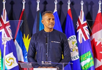 President Best stands behind a clear lectern with the 555th Annual Meeting branding delivering remarks. Behind him, flags of CDB member countries are displayed.