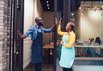 Side view of black man and woman smiling and doing high five to each other while opening cafe for customers