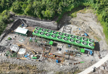 Aerial view of a geothermal power plant in Dominica under construction, surrounded by forested hills and heavy equipment on site.