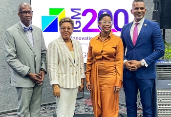 a group of four black persons two males one in a grey suit and another in a blue suit flanking two ladies one in white and one in orange all standing looking ahead 
