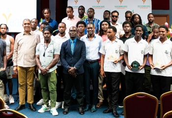 large group of predominantly male participants standing in front of a stage at an indoor venue 