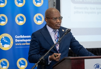 Black man in blue business suit at lectern in front of a multicolored backdrop