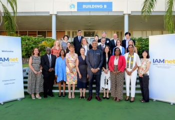 Group photo of participants at the IAMnet 2025 Annual Meeting in Bridgetown, Barbados, standing in front of Building B with event banners on both sides.