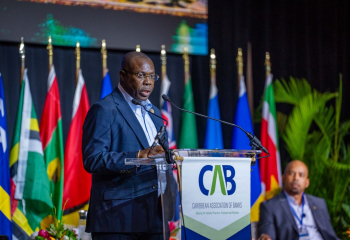 Dr Isaac Solomon in business suit standing at a branded lectern delivering remarks on stage 
