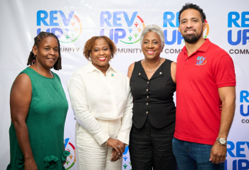 Three black women and one black man standing in a row looking ahead and smiling 