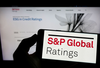 Person holding cellphone with logo of US financial services company SP Global Inc on screen in front of business webpage. Focus on phone display