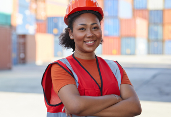 Female worker in hard hat smiling with arms crossed.