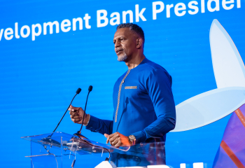 President of the Caribbean Development Bank, Mr. Daniel M. Best, speaks at a podium with microphones against a bright blue conference backdrop.