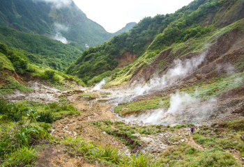 Clouds of geothermal steam rise from the ground in a mountainous area.