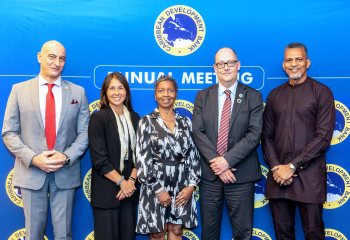 group of five persons standing in a row in business attire in front of a colourful back drop two women three men