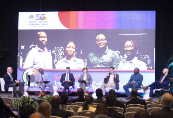Panelists seated on stage in front of screen with image of group