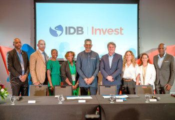 Nine delegates from CDB and IDB Invest pose behind a conference table beneath an IDB Invest backdrop at a formal partnership event.