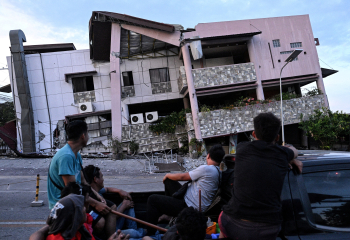 Passengers riding on the cargo bed of a pickup truck look at a damaged building a day after a magnitude 7.5 earthquake struck Caracas, causing widespread destruction and infrastructure damage