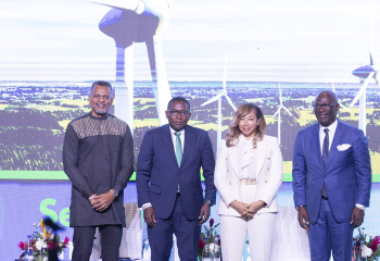 Four speakers standing on a stage in front of a wind turbine backdrop at The Breakfast Exchange: A Climate Talk on the Global Economy