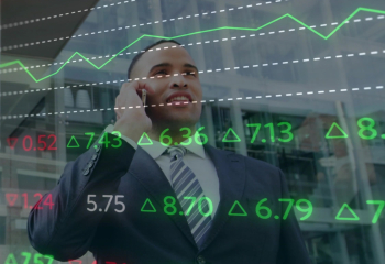 Businessman in suit looking up while talking on his cellphone with stock market numbers superimposed over image