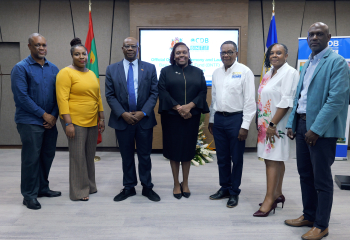 Three women and four men appear at the front of a meeting room for the launch of a new Caribbean Development Bank project in Grenada
