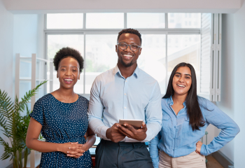 Three smiling young professionals stand together.