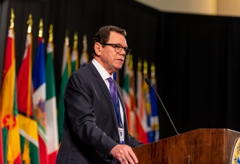 Dr. Warren Smith standing at lectern in black suit with mauve tie