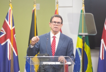 CDB President Dr Wm Warren Smith wearing blue suit and red tie, standing at a transparent lectern