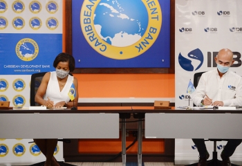 CDB VPO seated left in white dress and IDB IDB Representative in Barbados seated left in white. CDB and IDB branding is in the background