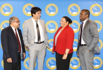 Four people wearing suits talk to each other, smiling, against a background featuring CDB's logo