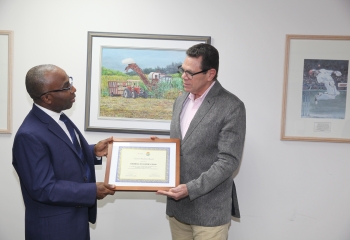 Dr Yves Personna in blue suit presenting award to Dr Warren Smith in grey jacket.