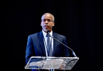 Luther St. Ville in dark suit and white shirt at lectern