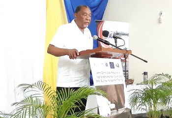 older gentleman in white shirt and black slacks standing at a wooden lectern