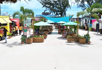 colourful beach stalls with white sand, customers and blue umbrellas, white sand and string lighting