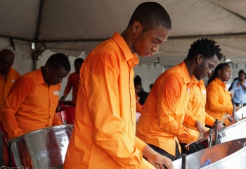 Men in orange shirts playing steelpan.