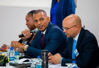 Daniel Best in navy suit sitting at head table speaking into microphone.