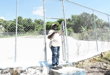 Trenail resident in white shirt and blue trousers stands at the open gate to water catchment facility