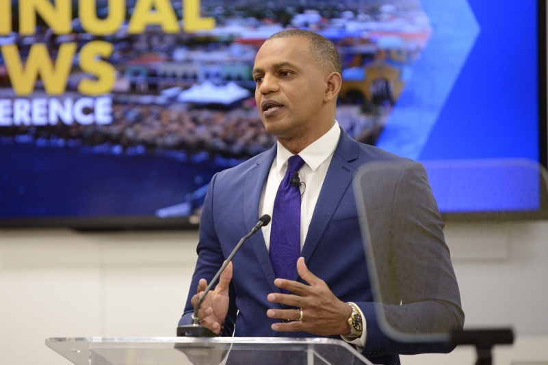 Daniel Best wearing a blue suit, white shirt and a purple tie standing at the lectern