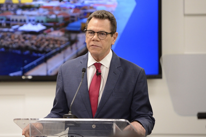 Dr. Warren Smith in a blue suit, white shirt and red tie standing at lectern