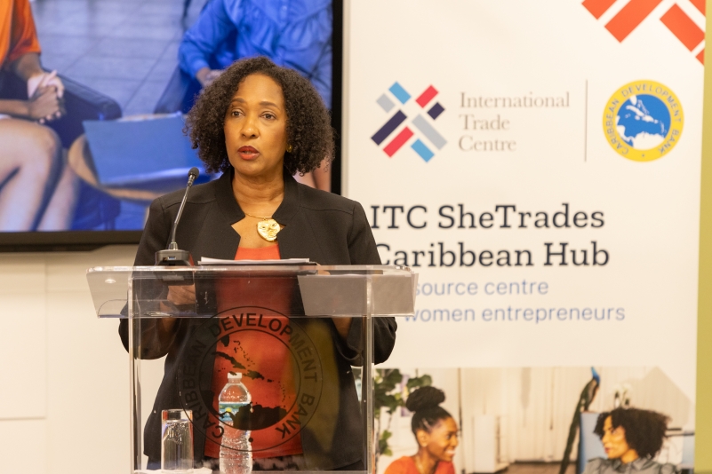 black woman in red maroon dress with black business jacket standing at lectern