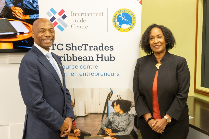 photo of male in grey business suit and female in maroon dress with black business jacket standing in front of branded backdrop