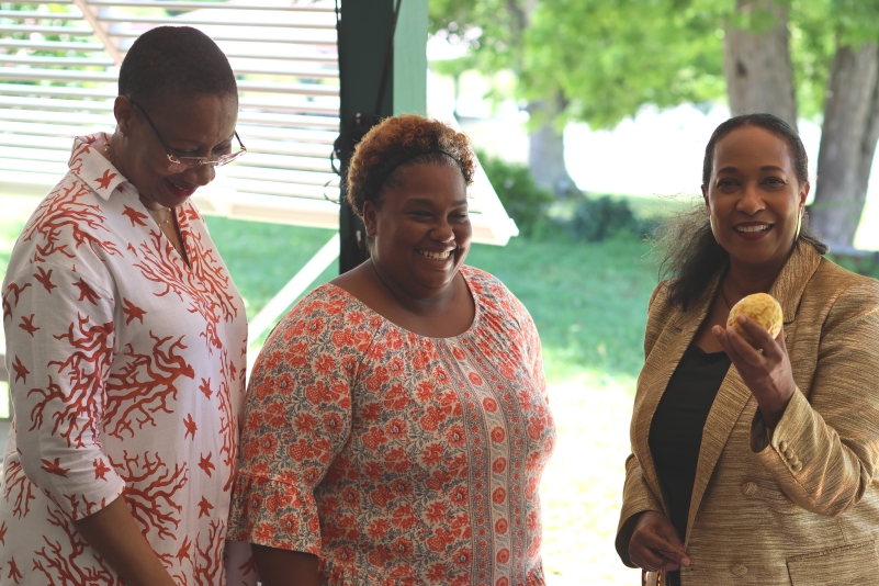 two black women looking down and one black woman holding a fruit looking at the camera
