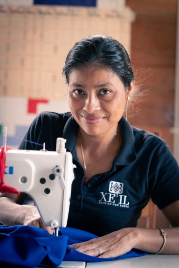 One Mayan woman in a black top seated behind a white sewing machine sewing