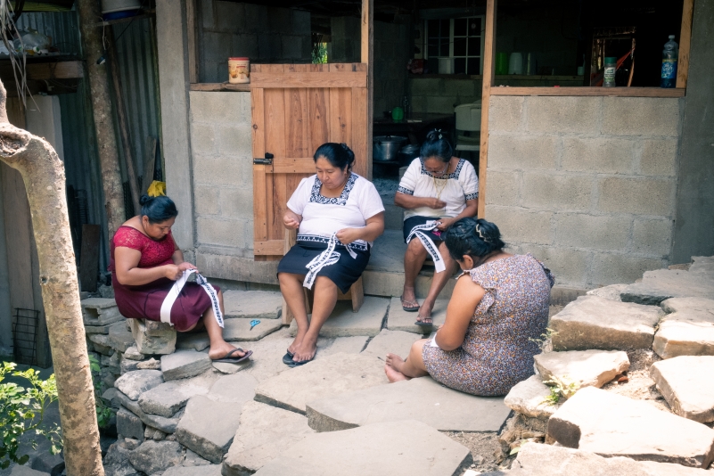 Four Mayan women seated outdoors hemstitching Mayan garments