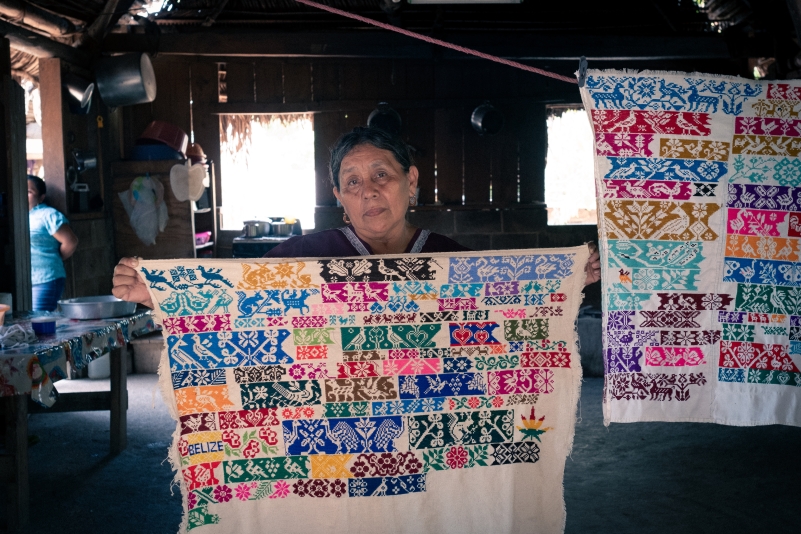 One Mayan woman holding up brightly coloured embroidered designs 