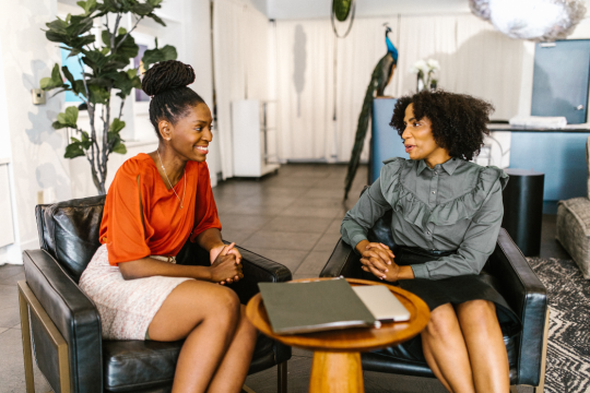 two young females in business attire seated having a discussion